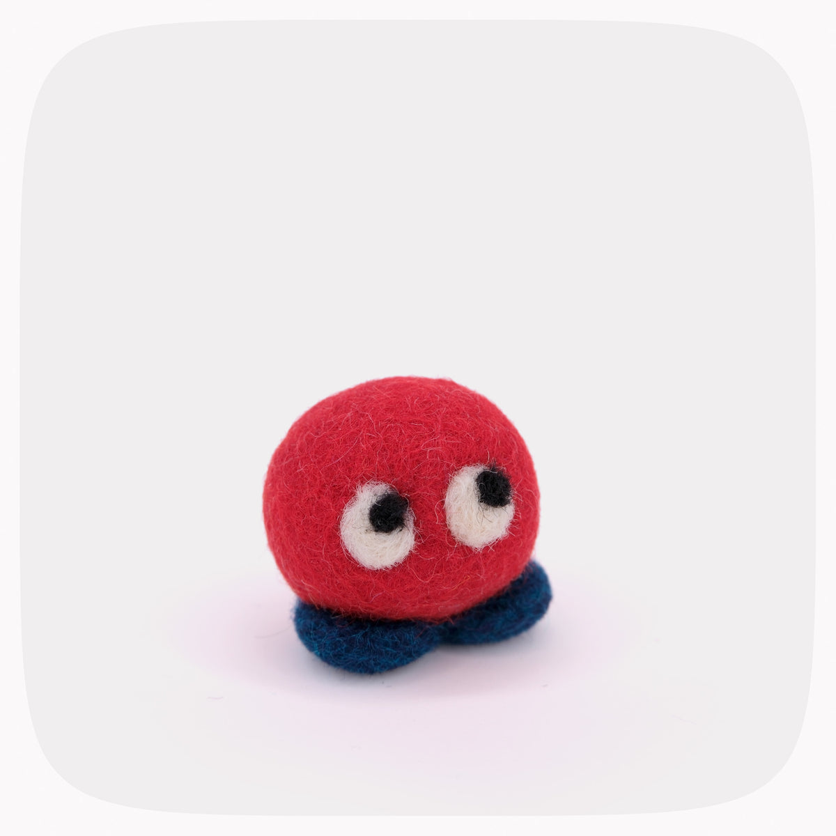 A small felt toy creature with a round red body, large white eyes with black pupils, and two dark blue felt legs, centered on a light gray background.