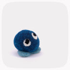 A small blue felt plush toy with a round fuzzy body, two large white-and-black embroidered eyes, and two short blue felt feet, shown on a light gray background.