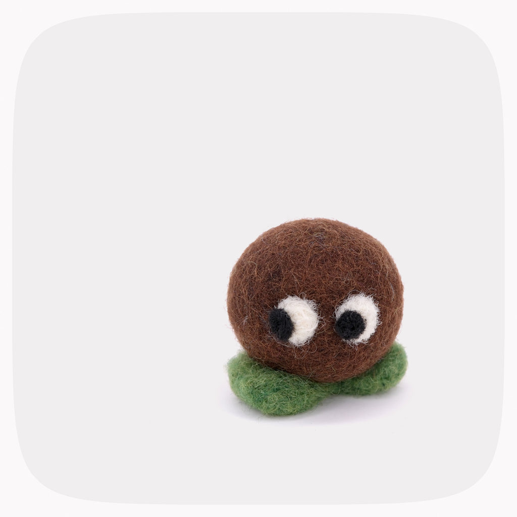 A small felt toy character with a round brown head, white and black eyes, and a green felt base, centered on a light gray background with rounded corners.