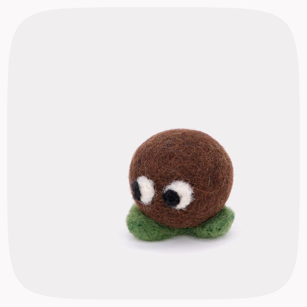 A small felt toy character with a round brown head, white and black eyes, and green felt feet, centered on a light gray background with rounded corners.