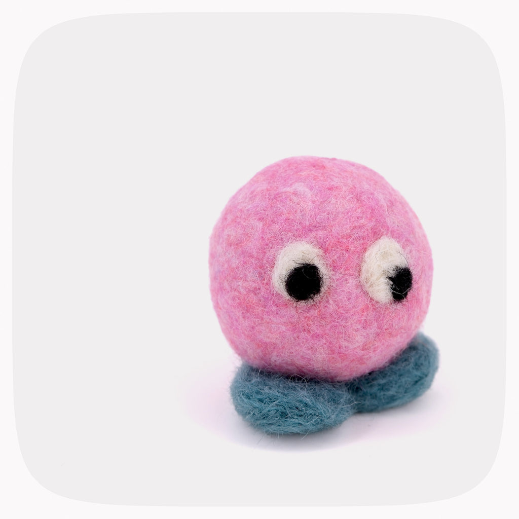 A pink felt toy with large white and black eyes and a blue-green feet, centered on a light gray background with rounded corners.