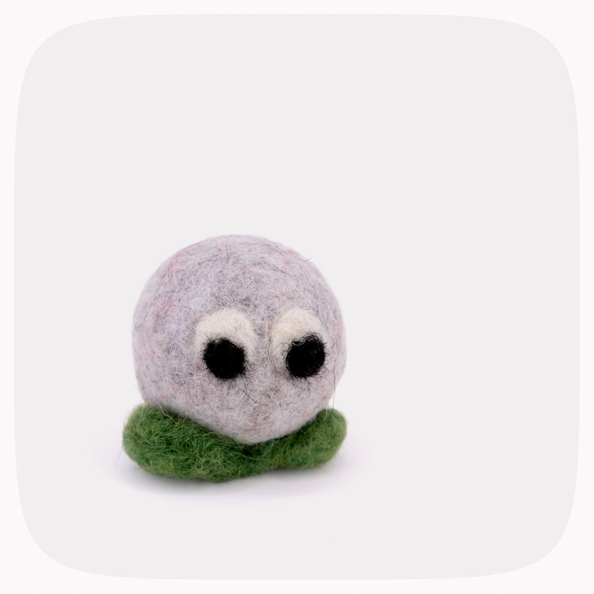 A small felted wool toy character with a round light gray head, large black eyes with white highlights, and a green felted base, shown on a plain light gray background.
