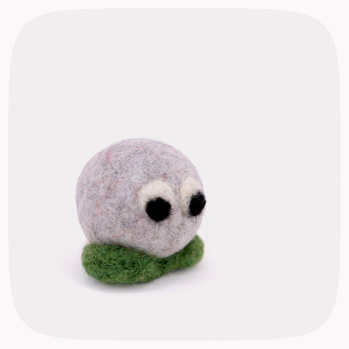 A small felt figurine with a light gray felted body, black and white eyes, and a green felt leaf base, shown on a light gray background with rounded corners.