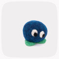 A small felted wool character toy with a round blue body, green feet, and large white eyes with black pupils, centered on a light gray background.