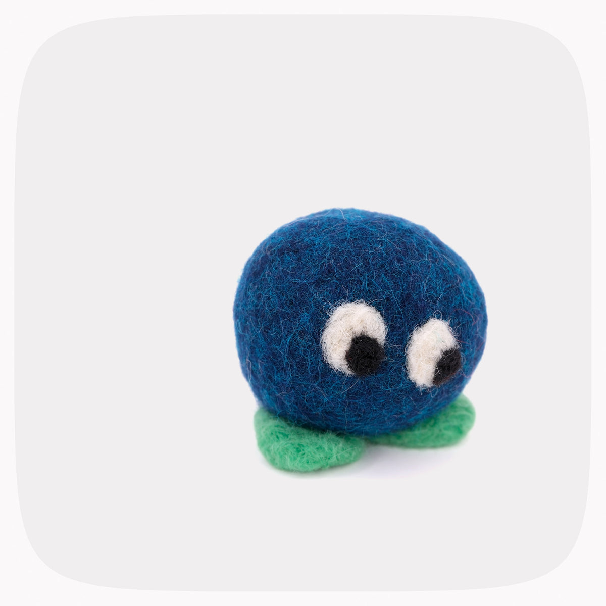 A small felted wool character toy with a round blue body, green feet, and large white eyes with black pupils, centered on a light gray background.