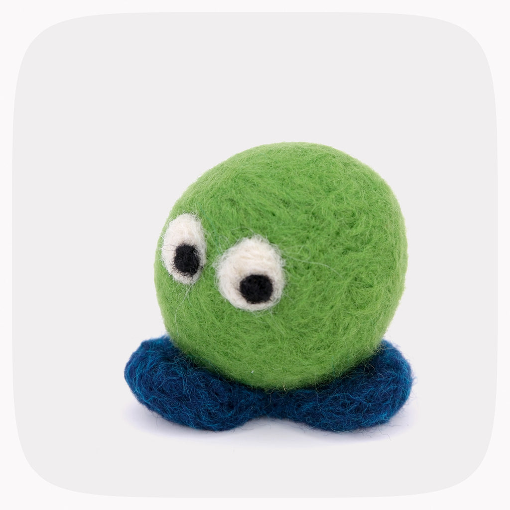 A small felted wool toy with a round green head, two large white eyes with black pupils, and dark blue feet centered on a light gray rounded-square background.