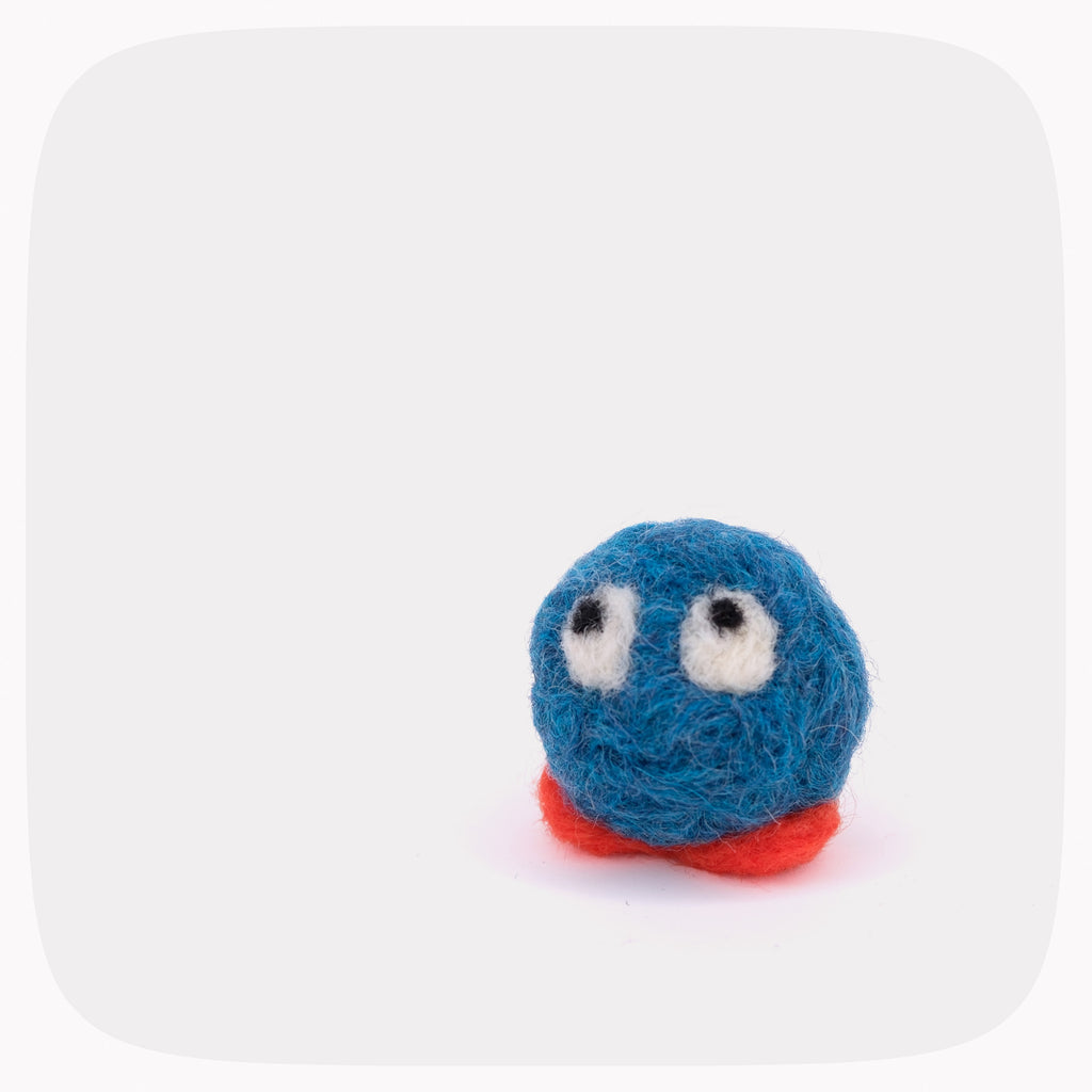 A small blue felt character toy with white eyes and a red base, photographed on a clean white background with rounded corners.
