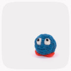 A small blue felt character toy with white eyes and a red base, photographed on a clean white background with rounded corners.
