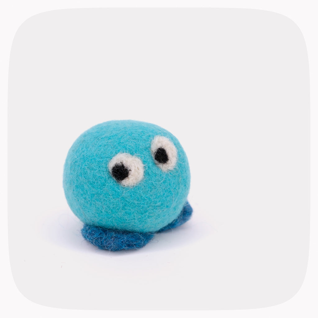 A small felt toy in bright turquoise blue with dark blue feet, white and black eyes, and white felt cheeks, photographed on a light gray background with rounded corners.