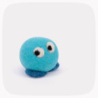 A small felt toy in bright turquoise blue with dark blue feet, white and black eyes, and white felt cheeks, photographed on a light gray background with rounded corners.