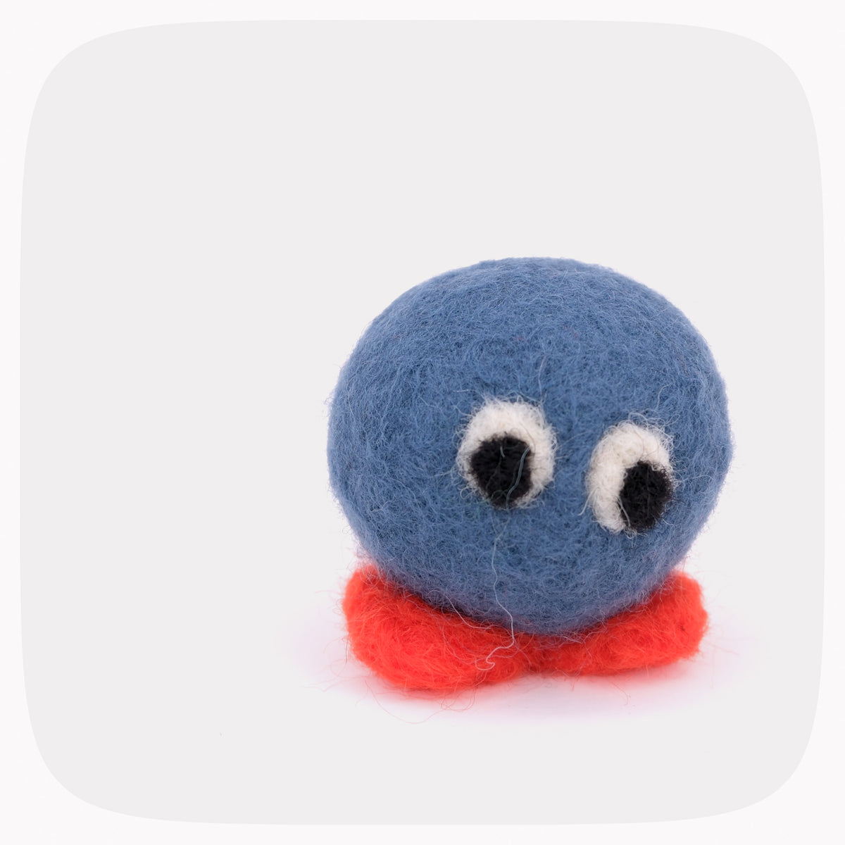 A small felt toy character with a round blue head, large white and black eyes, and a red base, photographed on a plain light gray background.