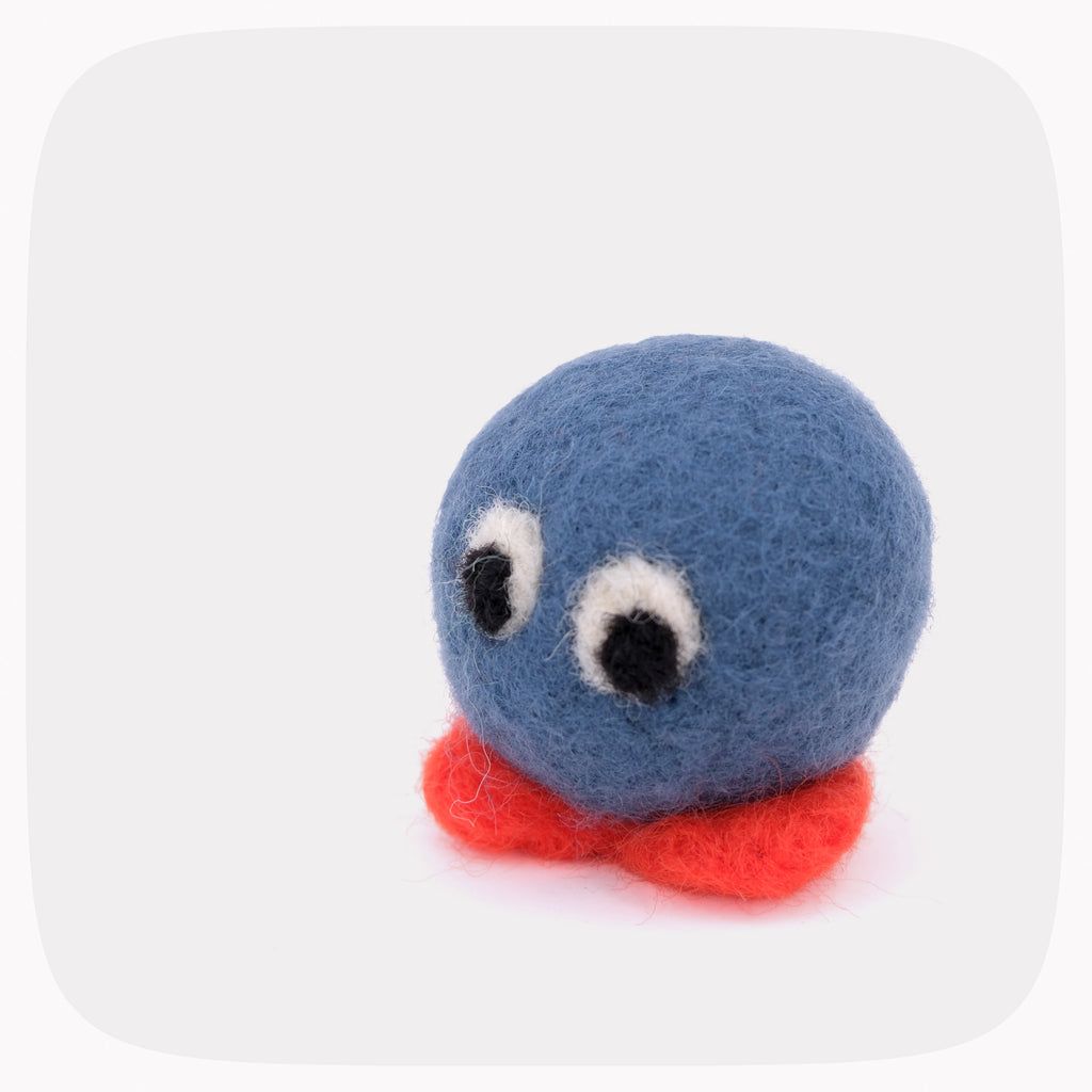 A small felt toy character with a round blue head, large white eyes with black pupils, and a red body, photographed on a light gray background with rounded corners.