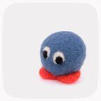 A small felt toy character with a round blue head, large white eyes with black pupils, and a red body, photographed on a light gray background with rounded corners.