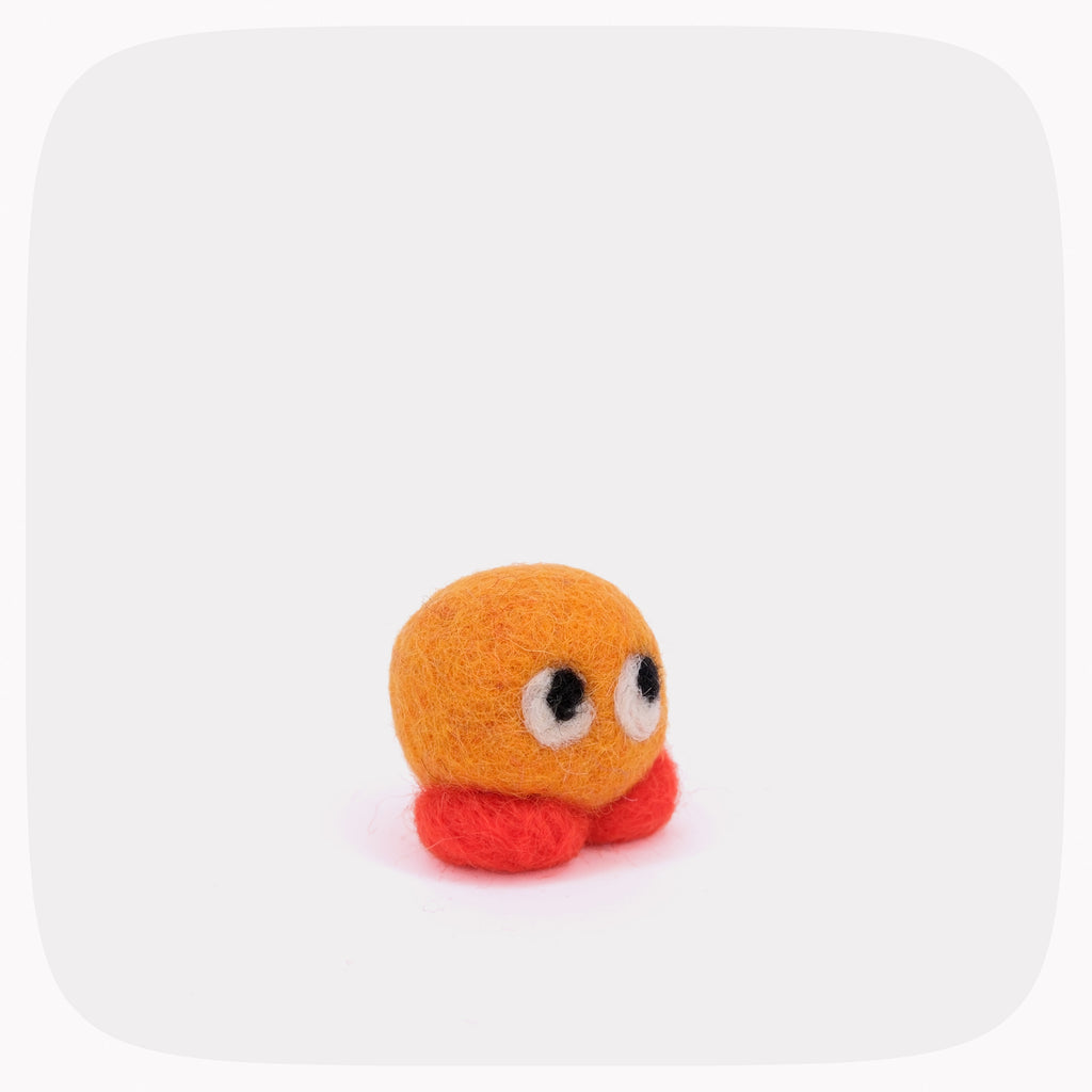 A small orange felt toy character with large white eyes and red feet, centered on a light gray rounded-square background.