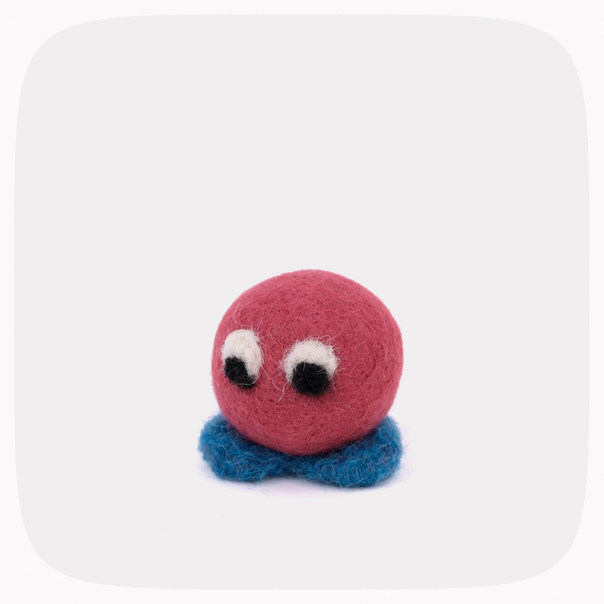 A small felted wool toy character with a round pink head, white and black bead eyes, and fuzzy blue feet, centered on a light gray rounded-square background.