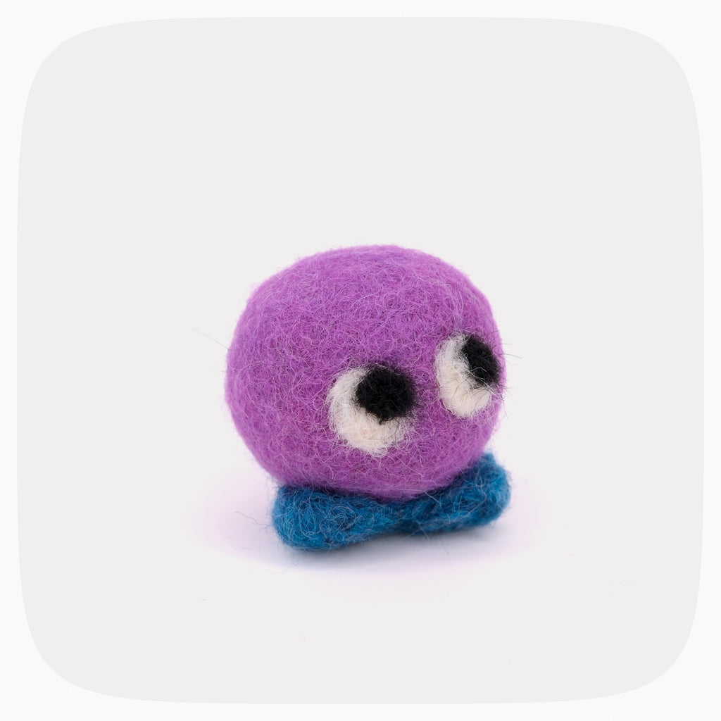A small felted wool creature toy with a round purple head, large white and black eyes, and a blue textured base, centered on a light gray background with rounded corners.