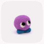 A small felted wool creature toy with a round purple head, large white and black eyes, and a blue textured base, centered on a light gray background with rounded corners.