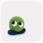 A small felted wool toy with a bright green round body, dark blue feet, and large white eyes with black pupils, centered on a light gray background with rounded corners.