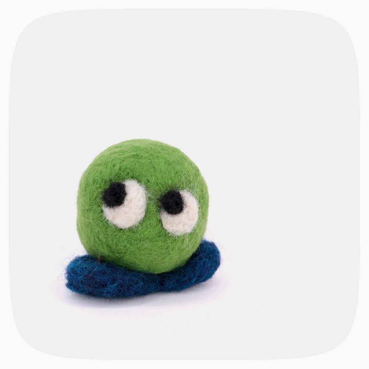 A small felted wool toy with a bright green round body, dark blue feet, and large white eyes with black pupils, centered on a light gray background with rounded corners.