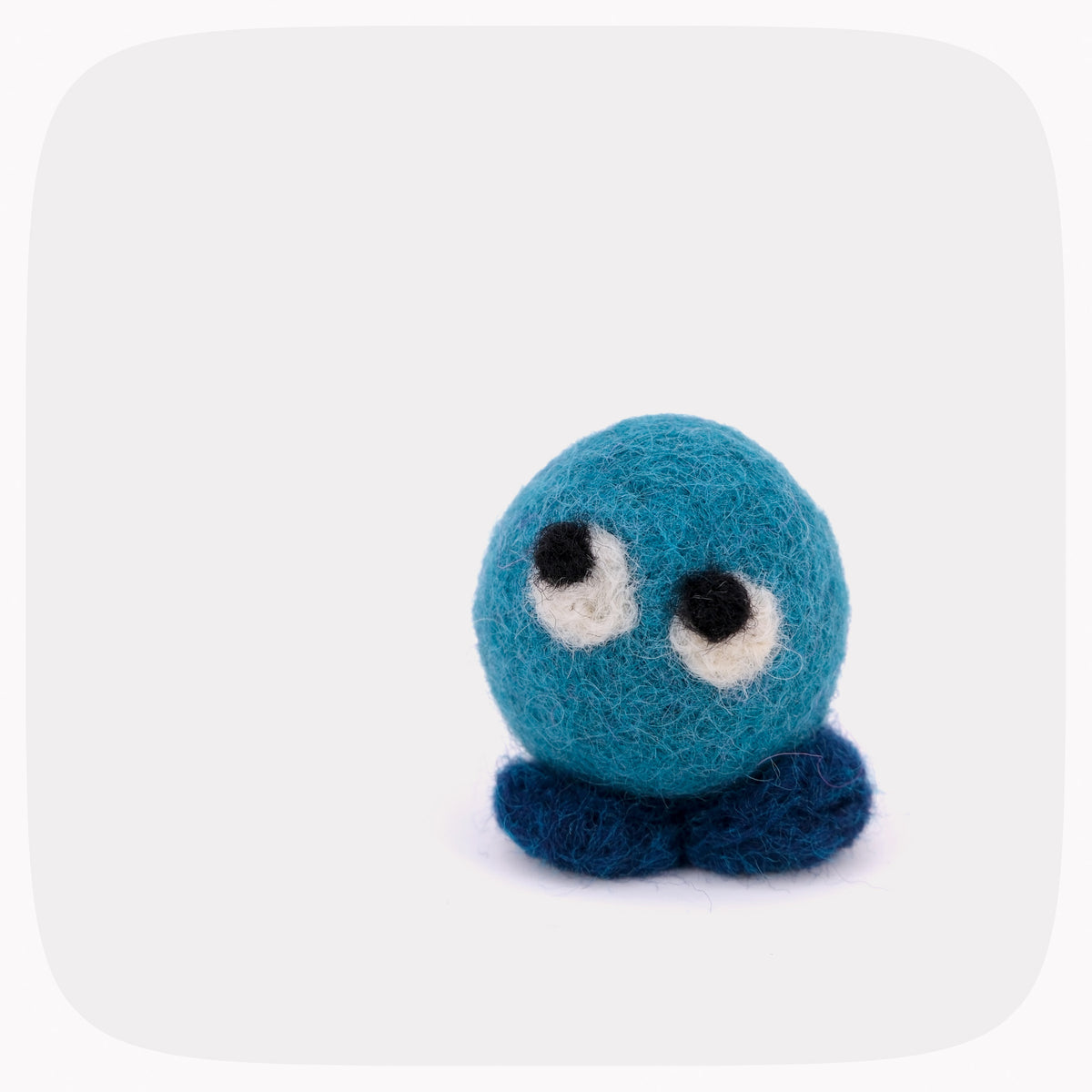 A small felted wool toy with a teal blue round body, dark blue feet, and large white eyes with black pupils, centered on a light gray background with rounded corners.