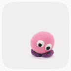A small felt toy with a pink round body, purple feet and large googly-style eyes, photographed on a light gray background with rounded corners.