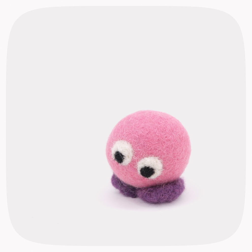 A small felt toy with a pink round body, purple feet and large googly-style eyes, photographed on a light gray background with rounded corners.