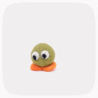 A small felt toy character with an olive green round body, two large white googly eyes with black pupils, and two orange felt legs, centered on a light gray rounded-square background.