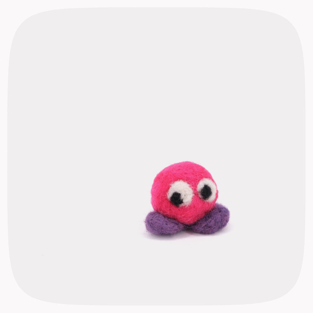 A small felted pink ball with purple feet and eyes looking left.