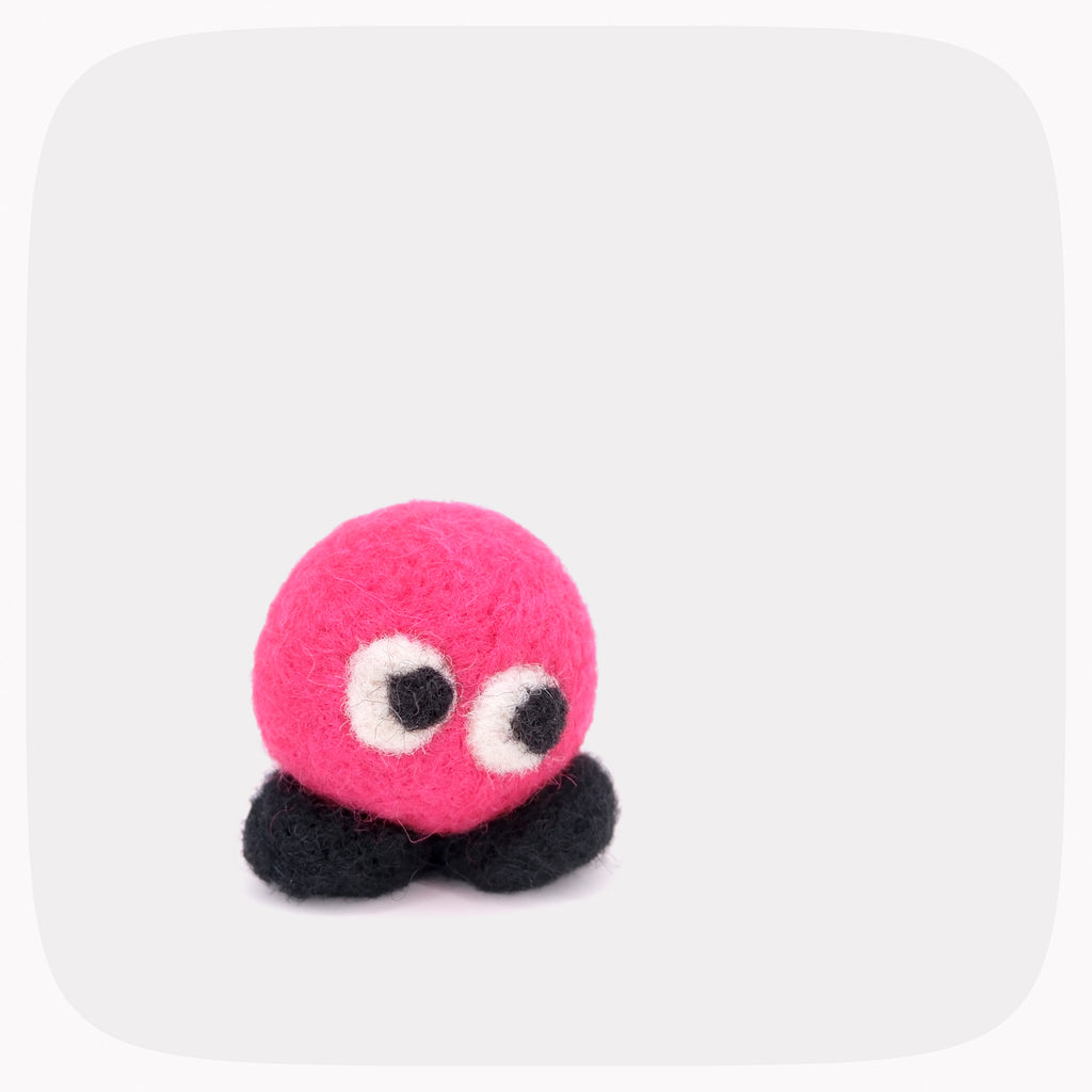 A small neon pink round felted character with black feet.