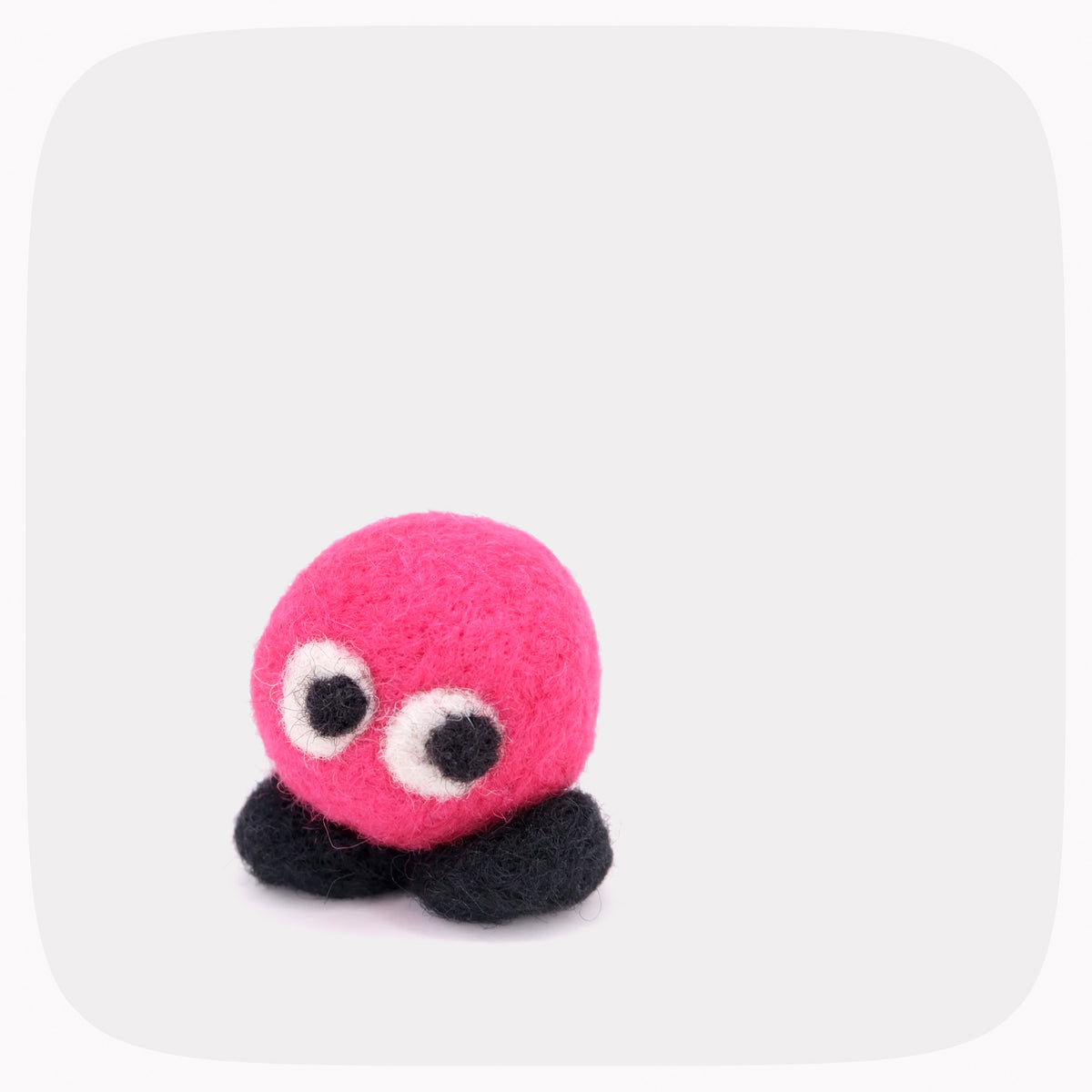 A small neon pink round felted character with black feet.