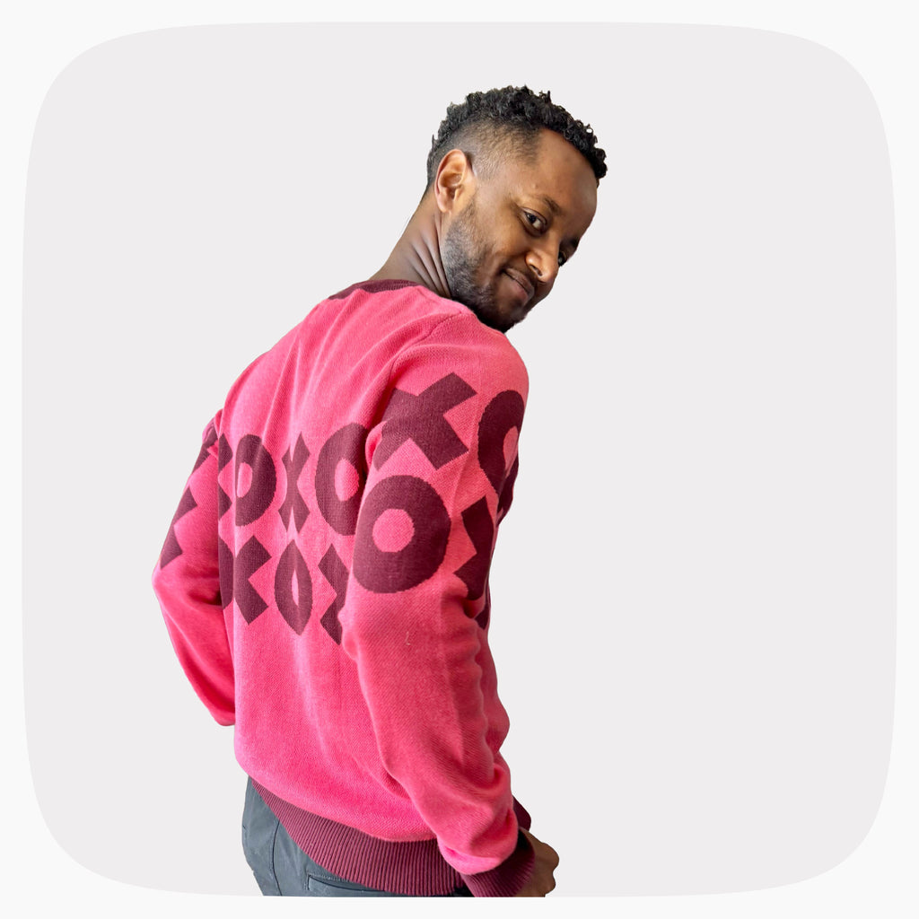 A man wearing A pink graphic knit sweater with a dark red XOXO pattern across the chest and back