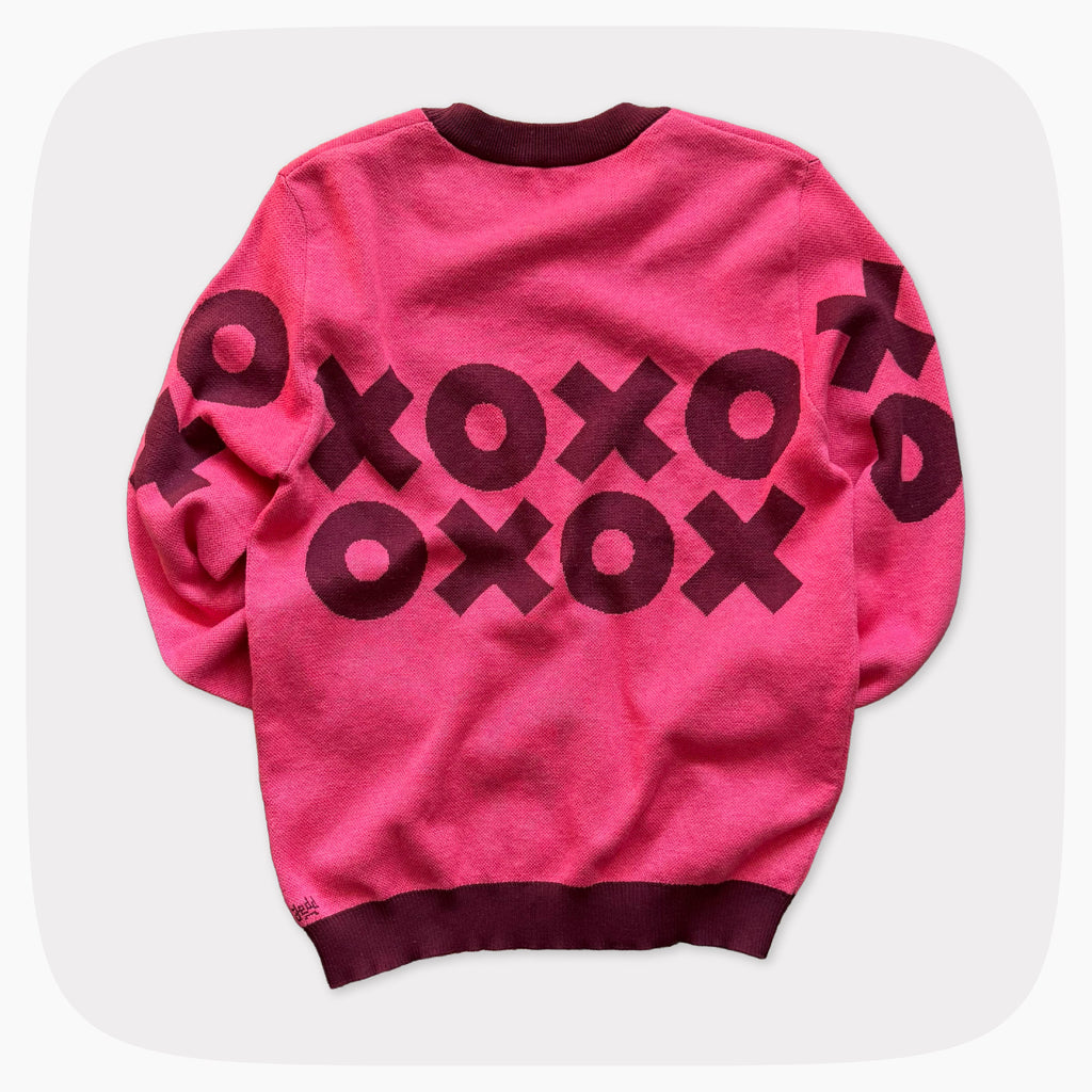 The back view of A pink graphic knit sweater with a dark red XOXO pattern across the chest.