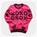 A pink graphic knit sweater with a dark red XOXO pattern across the chest.