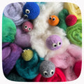 A close-up arrangement of colorful wool roving and small felted yarn balls with googly eyes, filling the frame on a rounded-square background.