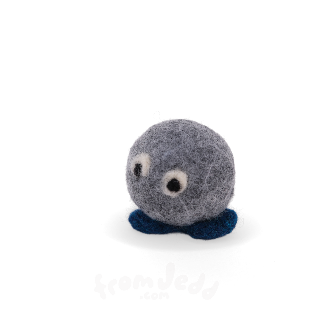 A small felted wool sculpture character with a round gray body, dark blue feet, and two white-and-black bead eyes, photographed on a clean white background.