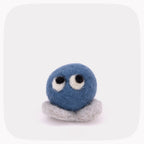 A blue felted circle with eyes and gray feet.