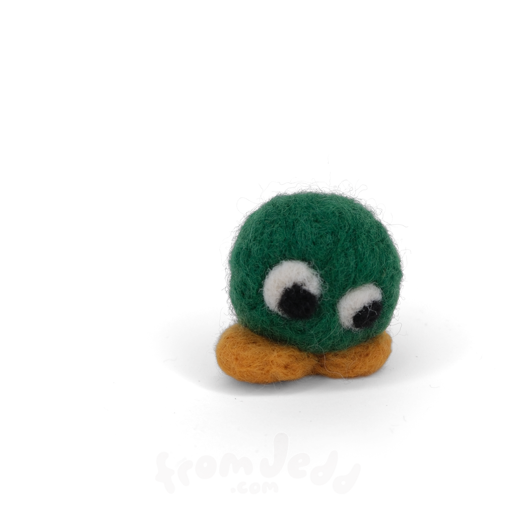 A small felted wool character toy with a round green head, large white eyes with black pupils, and a rounded orange base, photographed on a clean white background.