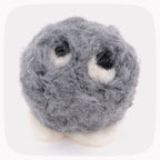 A gray fuzzy felted ball with eyeballs looking up and white feet.