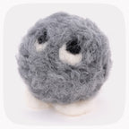 A gray fuzzy felted ball with eyeballs looking up and white feet.