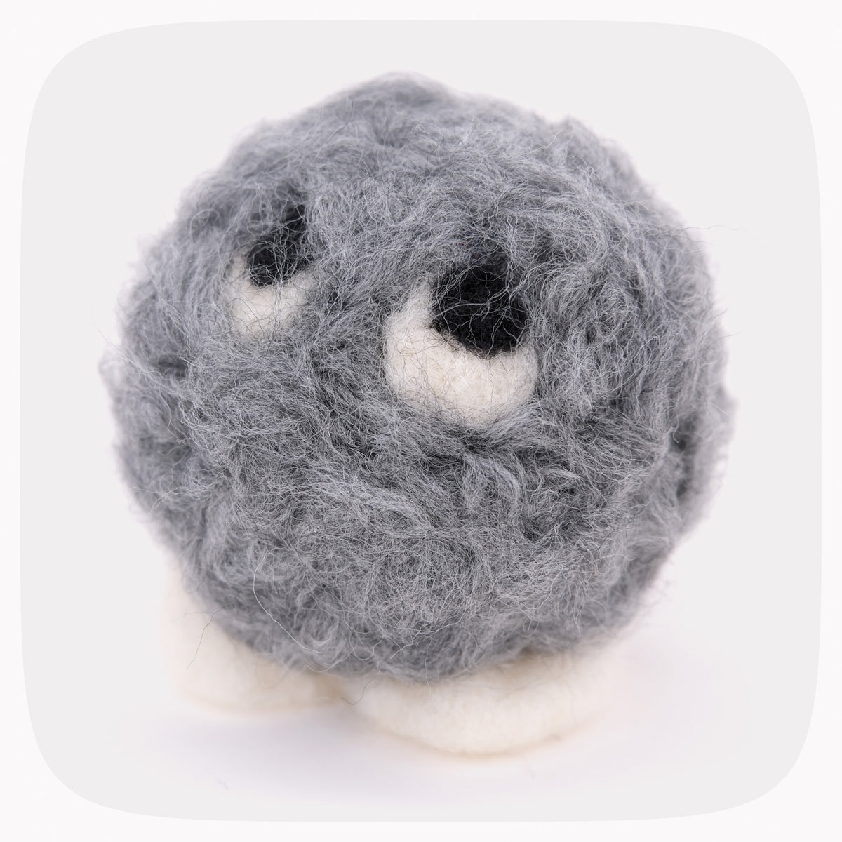 A gray fuzzy felted ball with eyeballs looking up and white feet.