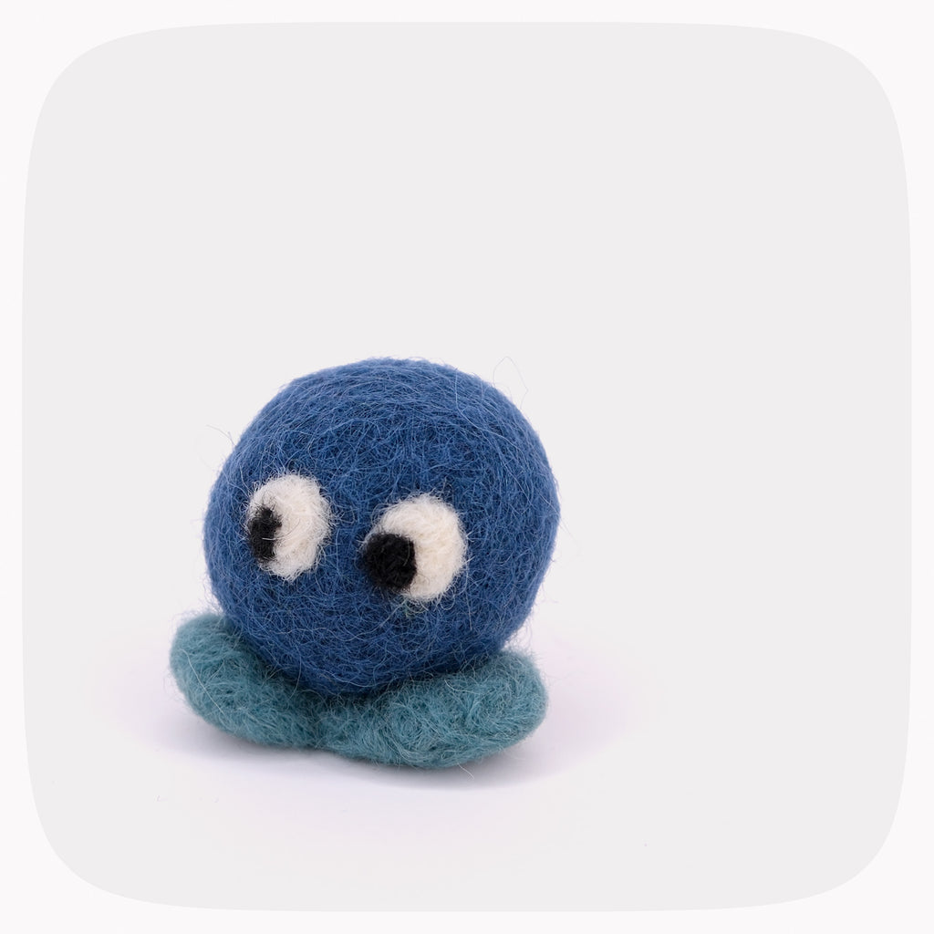 A blue felted ball with eyes looking down with lighter blue feet.